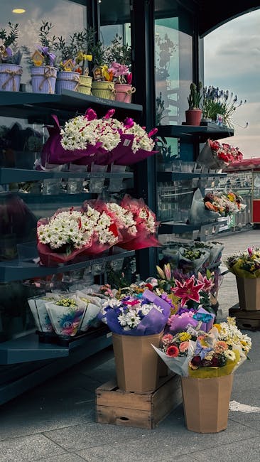 A display of various floral arrangements and bouquets at a florist shop, featuring vibrant pink, white, purple, and yellow flowers. The arrangements include chrysanthemums, roses, lilies, and mixed se