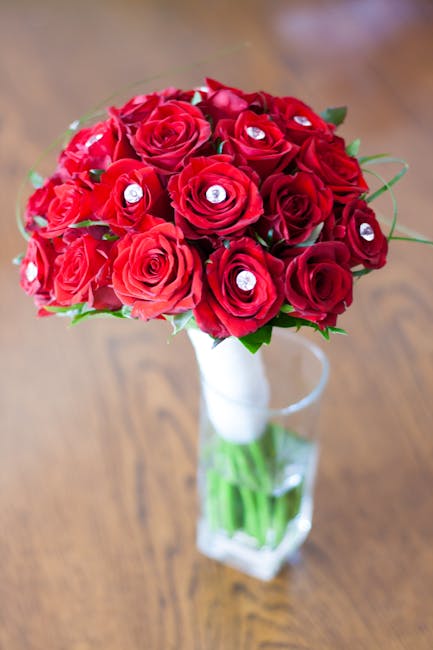A bouquet arrangement of fresh red roses and deep pink roses, elaborately styled in a round, lush cluster. The roses are perfectly opened, displaying velvety petals with a slight sheen, accented by sm